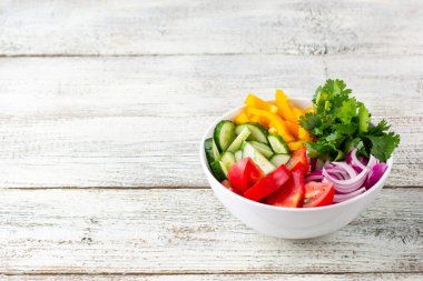 Farklı sebzelerle dolu bir tabak gökkuşağı salatası ve beyaz ahşap arka planda beyaz kâse içinde otlar. Kopyalama alanı ile