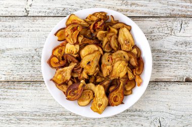 Ahşap arka planda beyaz bir tabakta dilimlenmiş kuru armut yığını. Kurutulmuş meyve cipsi. Sağlıklı yiyecekler. Üst görünüm