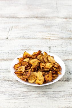 Ahşap arka planda beyaz bir tabakta dilimlenmiş kuru armut yığını. Kurutulmuş meyve cipsi. Sağlıklı vejetaryen yemekleri.