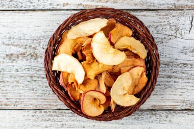 Hasır sepette beyaz ahşap arka planda kurumuş elma dilimleri yığını. Kurutulmuş meyve cipsi. Sağlıklı yiyecekler. Üst görünüm