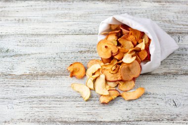 Ahşap arka plandaki beyaz bir keseden alınmış kurumuş elma hapları yığını. Kurutulmuş meyve cipsi. Sağlıklı vejetaryen yemekleri