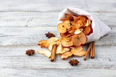 Ahşap arka plandaki beyaz bir keseden bir yığın kurutulmuş elma ve baharat hapı. Kurutulmuş meyve cipsi. Sağlıklı vejetaryen yemekleri