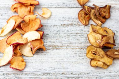 Beyaz ahşap arka planda dilimlenmiş kuru armut ve elma yığınının sınırı. Kurutulmuş meyve cipsi. Sağlıklı yiyecekler. Üst görünüm
