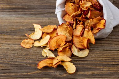 Ahşap arka plandaki beyaz bir keseden alınmış kurumuş elma hapları yığını. Kurutulmuş meyve cipsi. Sağlıklı vejetaryen yemekleri