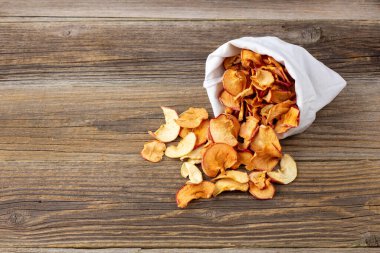 Ahşap arka plandaki beyaz bir keseden alınmış kurumuş elma hapları yığını. Kurutulmuş meyve cipsi. Sağlıklı vejetaryen yemekleri