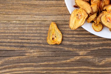 Ahşap arka planda beyaz bir tabakta dilimlenmiş kuru armut yığını. Kurutulmuş meyve cipsi. Sağlıklı yiyecekler. Kopyalama alanı olan üst görünüm
