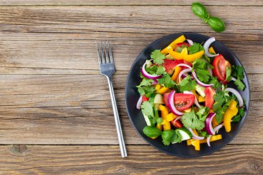 Farklı sebzelerle dolu bir tabak gökkuşağı salatası ve siyah tabakta doğal ahşap zemin çatallı otlar. Kopyalama alanı olan üst görünüm