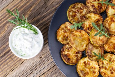 Ekşi krema soslu kızarmış kabak dilimleri. Doğal kahverengi ahşap arka planda akşam yemeği için otlu kızarmış kabaklar. Üst Wiev