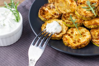 Ekşi krema soslu kızarmış kabak dilimleri. Doğal kahverengi ahşap arka planda akşam yemeği için otlu kızarmış kabaklar. Top wiev. Kapat.