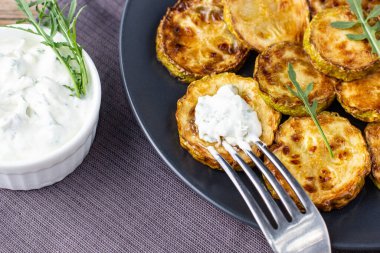 Ekşi krema soslu kızarmış kabak dilimleri. Doğal kahverengi ahşap arka planda akşam yemeği için otlu kızarmış kabaklar. Top wiev. Kapat.