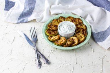 Ekşi krema soslu kızarmış kabak dilimleri. Beyaz arka planda akşam yemeği için otlu kızarmış kabaklar ve peçete.