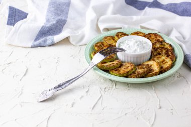 Ekşi krema soslu kızarmış kabak dilimleri. Beyaz arka planda akşam yemeği için otlu kızarmış kabaklar ve peçete.