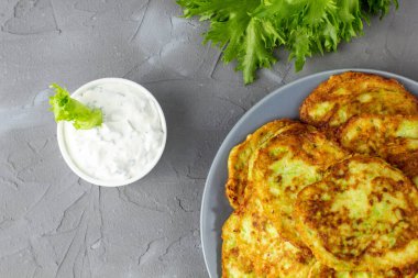 Ekşi krema soslu ve yeşillikli kabaklı börekler. Gri arka planda yeşil salatalı sebzeli gözleme. Üst görünüm