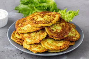 Ekşi krema soslu ve yeşillikli kabaklı börekler. Gri arka planda yeşil salatalı kabak krepleri..