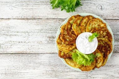 Ekşi krema soslu ve yeşillikli kabaklı börekler. Beyaz ahşap arka planda yeşil salatalı sebzeli gözleme. Kopyalama alanı olan üst görünüm