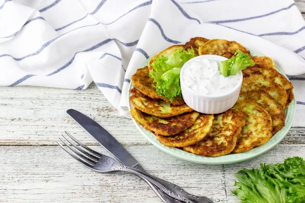 Ekşi krema soslu ve yeşillikli kabaklı börekler. Beyaz ahşap arka planda yeşil salatalı sebzeli gözleme..