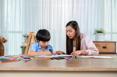 Asyalı anne oğluyla birlikte evde çalışıyor. Anne ve çocuk resim çiziyor ve resim boyuyor. Kadın yaşam tarzı ve aile aktiviteleri.