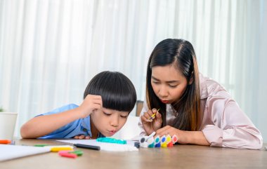 Asyalı anne oğluyla birlikte evde çalışıyor. Anne ve çocuk resim çiziyor ve resim boyuyor. Kadın yaşam tarzı ve aile aktiviteleri.