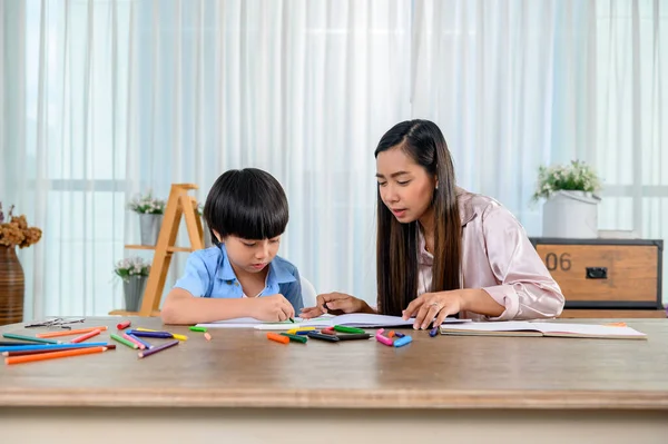 Asian mother work home together with son. Mom and kid drawing picture and color painting art. Woman lifestyle and family activity.