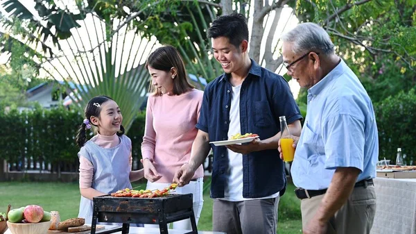 Asian family having a barbecue party at home. Cooking grilled bbq for dinner in backyard. Lifestyle on summer holiday.