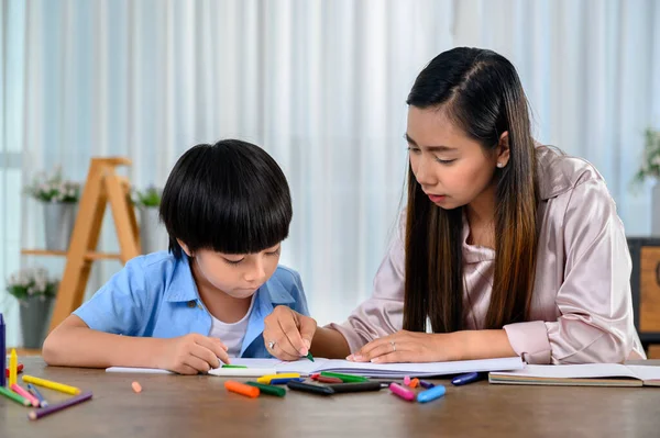 Asian mother work home together with son. Mom and kid drawing picture and color painting art. Woman lifestyle and family activity.