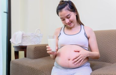 Asyalı hamile kadın evde yalnız kalıyor. Sağlıklı ve sağlıklı hamilelik için süt içen kadın.