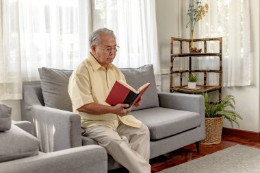 Asyalı kıdemli adam kitap okuyor ve evde yalnız kalıyor. Emeklilik yaşam tarzı.