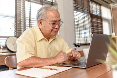 Asyalı kıdemli adam dizüstü bilgisayar kullanıyor ve emeklilikten sonra sigorta arıyor. Büyükbaba evde tek başına kal..