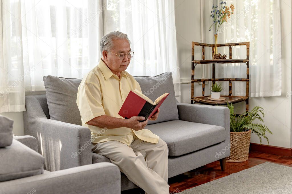 Asian Senior man reading book and stay alone at home. Retirement age lifestyle.