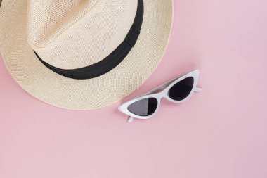 Sahilde pembe arka planda çekilmiş gibi görünen bir sahnede güneş şapkası ve güneş gözlüğü. En üst görüntü.
