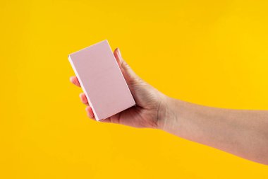 Küçük pembe bir hediye paketi ve sarı bir arka plana karşı el..