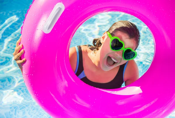 Happy teenager playing on a pink buoy in a pool with sunglasses — Stock Photo, Image