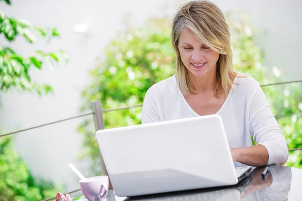 Усміхнена жінка працює на комп'ютері вдома з зеленим садом на її фоні — стокове фото