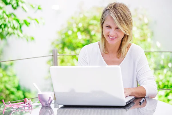 Lächelnde Frau, die zu Hause am Computer arbeitet, mit grünem Garten im Hintergrund — Stockfoto