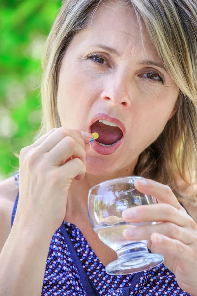Fechar-se de mulheres atraentes que tomam a medicina na pílula com vidro de água — Fotografia de Stock