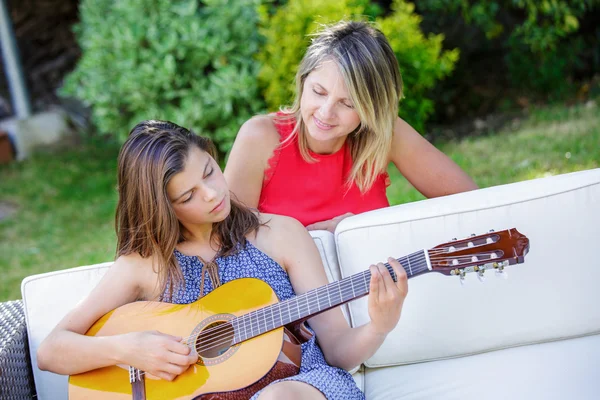 Söt flicka spela gitarr i en trädgård med hennes mamma — Stockfoto