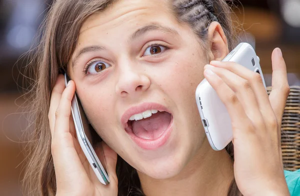Концептуальний портрет залежної молодої дівчини, що має анімовану розмову з телефоном в кожній руці — стокове фото