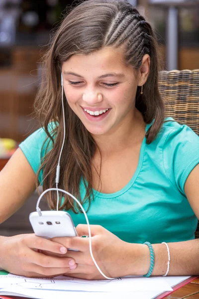 Гарненький студент робить домашнє завдання під час прослуховування музики на її телефоні — стокове фото