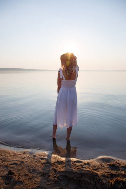 Kız, sırtı güneşe dönük halde suyun içinde duruyor.