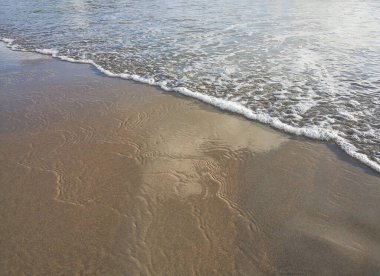 Yaz mevsimi deniz manzarası, yumuşak dalgalar ve kumsal. Dalgalar güneşli bir günde sahile çarpıyor.