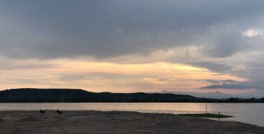Göl kenarında romantik bir gün batımı ve alacakaranlıkta bulutlu bir gökyüzü..