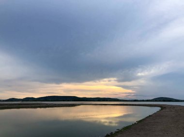 Göl kenarında romantik bir gün batımı ve alacakaranlıkta bulutlu bir gökyüzü..