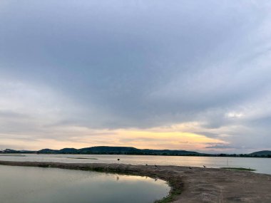 Göl kenarında romantik bir gün batımı ve alacakaranlıkta bulutlu bir gökyüzü..