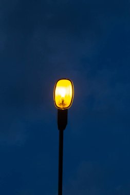 Gece vakti karanlık mavi gökyüzü arka planına turuncu ışık saçan sokak lambası seni yalnız hissettiriyor. Kopya alanı