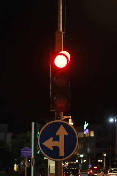 Traffic lights with red light for stop, road sign turn left and go ahead in town.
