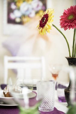 Boş gözlük, pasta ve bir buket çiçek masada.