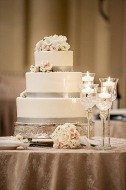 Düğün töreni. Üç katlı pasta. Beyaz kremalı ve gri süslemeli. Beyaz ve pembe güllerle süslenmiş.