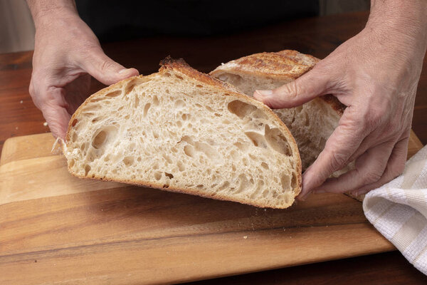 Homemade sourdough bread loaf being sliced on a cutting board by the chef, after being baked in the oven