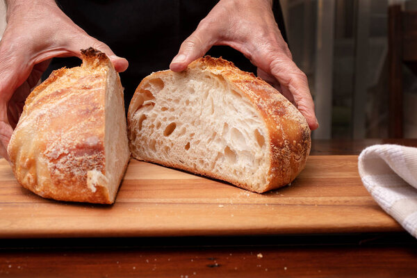 Homemade sourdough bread loaf being sliced on a cutting board by the chef, after being baked in the oven