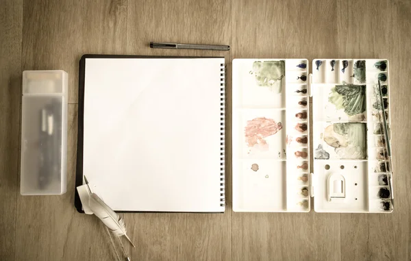 Top view of notebook and artist color palette on wood floor